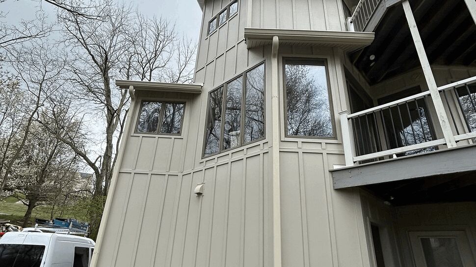 Tall board-and-batten siding with bay windows and downspout