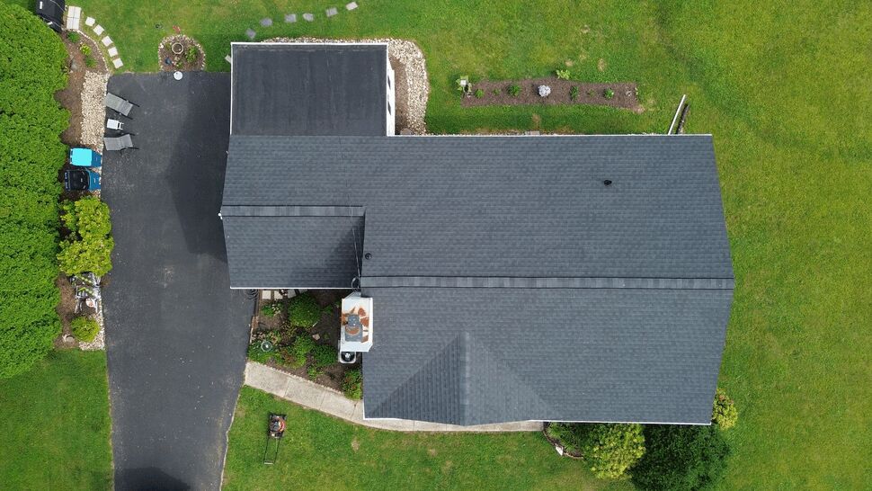 Top-down drone view of house roof showing full shingle coverage and driveway.