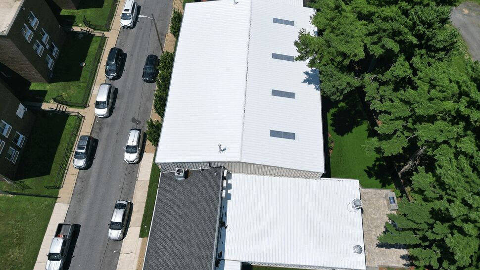Top-down view of a white commercial roof beside a street and parked cars.