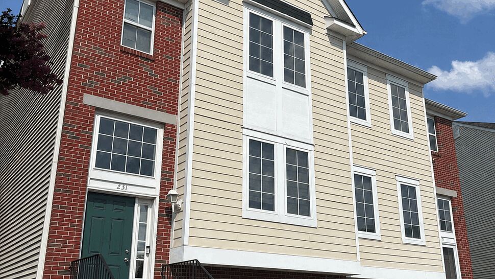Three-story townhouse with beige siding, brick facade, green doors and exterior stairs.