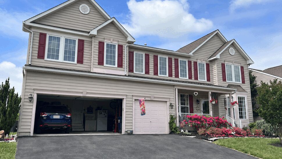 Two-story beige house with burgundy shutters, garage, and manicured front yard