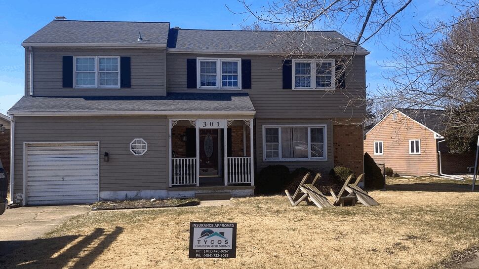 Front view of two-story house with a Tycos sign on the lawn under a clear blue sky