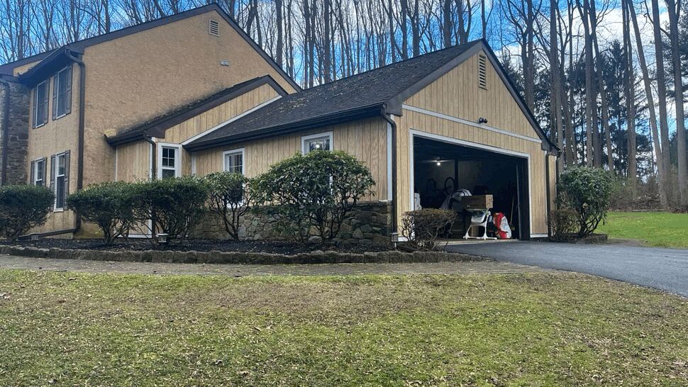Two-story home with attached garage, asphalt roof and front shrubs.