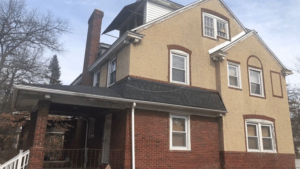 Corner view of two-story brick and stucco house with porch and gutters.