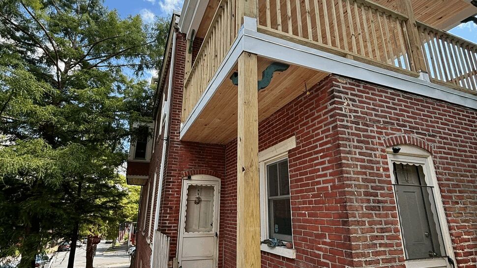 Two-story wooden deck with new posts and railing on brick house.