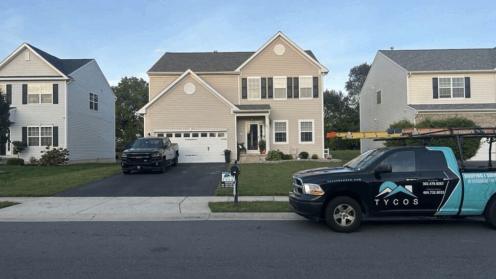 Company truck at residential roof | Tycos Roofing And Siding Inc Tycos Roofing And Siding Inc truck parked in front of a two-story suburban house
