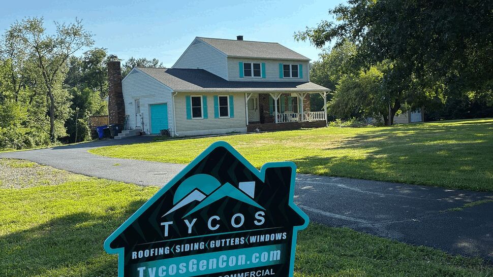 Yard sign for Tycos Roofing And Siding Inc in front of a two-story house
