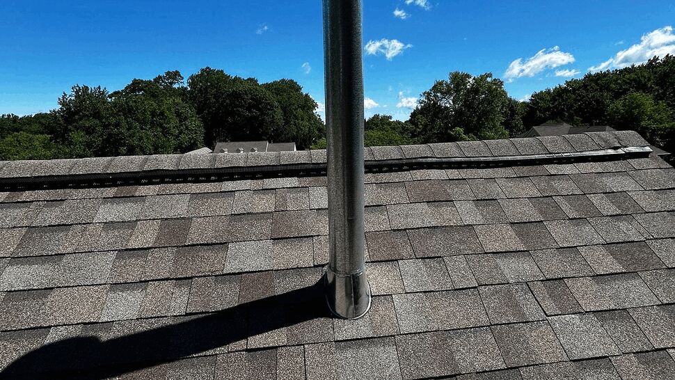 Vent pipe standing near ridge vent on shingled roof with blue sky