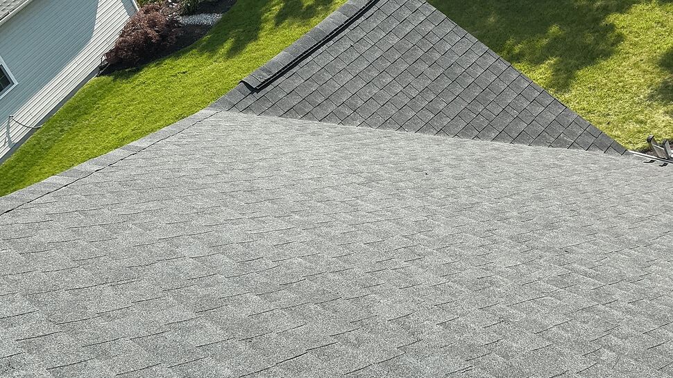Aerial view of gray shingle roof with Tycos Roofing trucks parked on the street