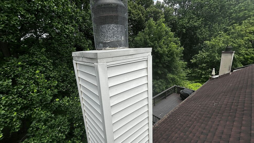 Vinyl-clad chimney chase with metal cap rising above the roof.