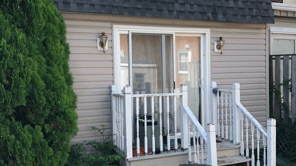Small rear porch with vinyl siding, sliding door, white railing and trash bin