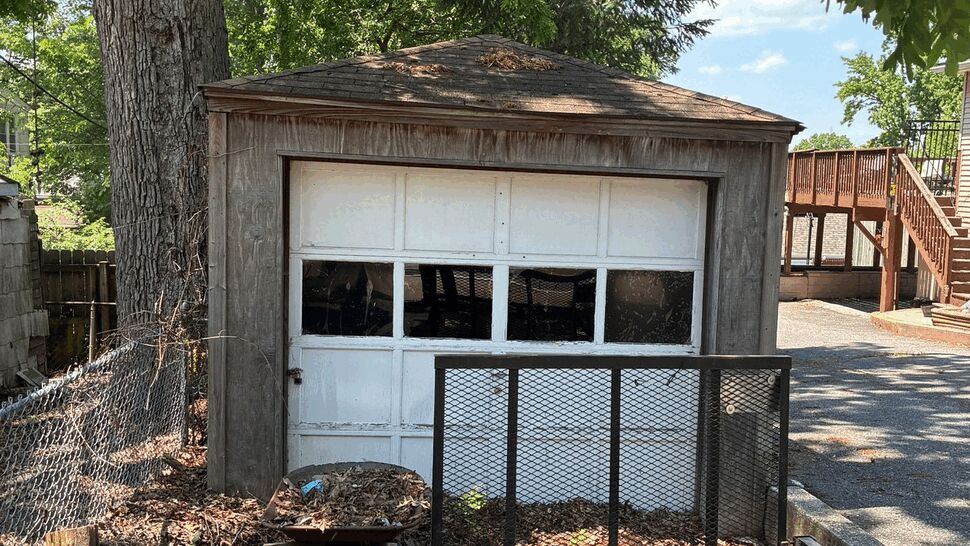 Old weathered garage with paneled white door and utility trailer in front