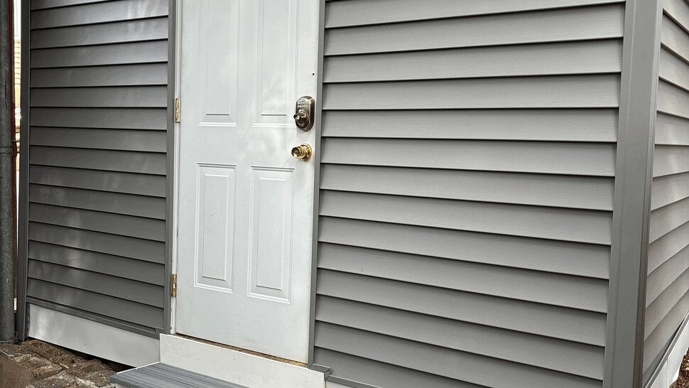 White exterior door with three steps and fresh gray vinyl siding