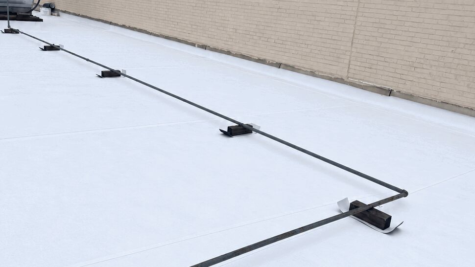 Flat roof anchor line installation | Tycos Roofing And Siding Inc Wide view of white flat roof showing anchor line and supports.