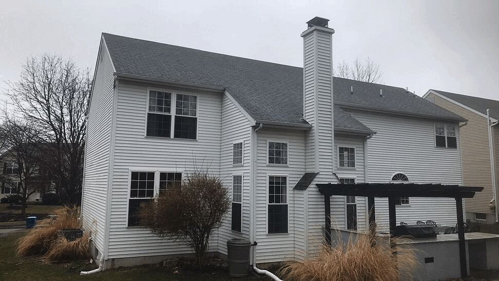 Rear view of white vinyl siding house with chimney, gutters and pergola over patio