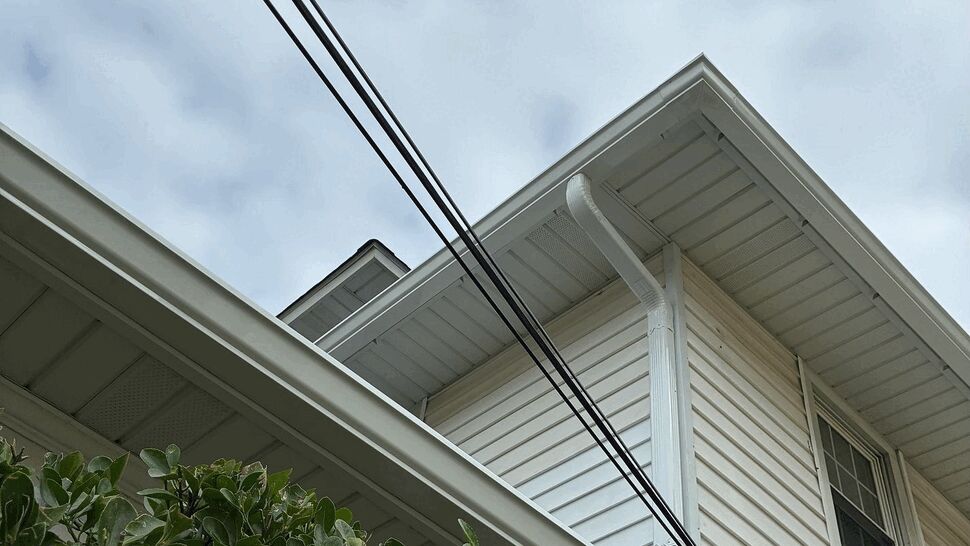White Siding and Gutter Detail | Tycos Roofing And Siding Inc White home siding, soffits, fascia, and downspout beneath a roof edge