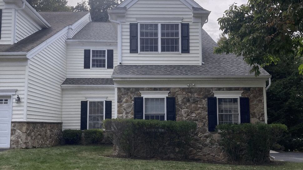 Two-story home with white siding, stone facade, black shutters and a shingled roof.