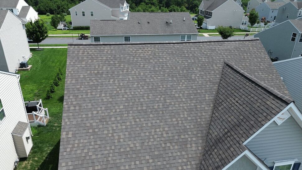 Wide aerial view of large shingled roof and surrounding neighborhood