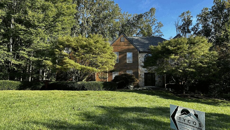 Two-story house with wood siding, roof visible and a Tycos sign on the lawn