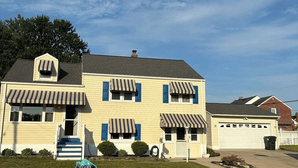 Yellow two-story house with blue shutters, striped awnings and a lawn sign.