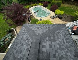 Aerial perspective of dark shingle roof above backyard pool and patio