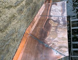 Shiny copper flashing over a window ledge on stone wall