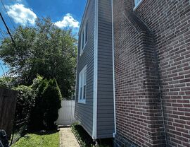 Narrow side yard walkway beside home with new gray siding and brick chimney