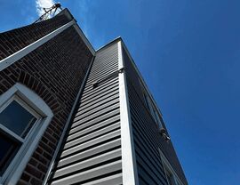 Low-angle view of house corner showing gray siding and roofline under clear sky