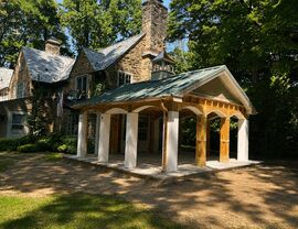 Wooden covered pavilion with columns next to stone house