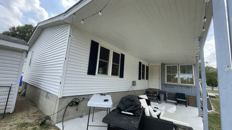 Covered patio beside a white-sided home with windows, seating, and outdoor grill