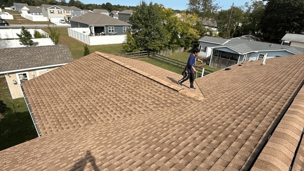 Residential Roofing Project | Top Roofing & Siding Worker walking across a large brown shingle roof in a residential neighborhood.