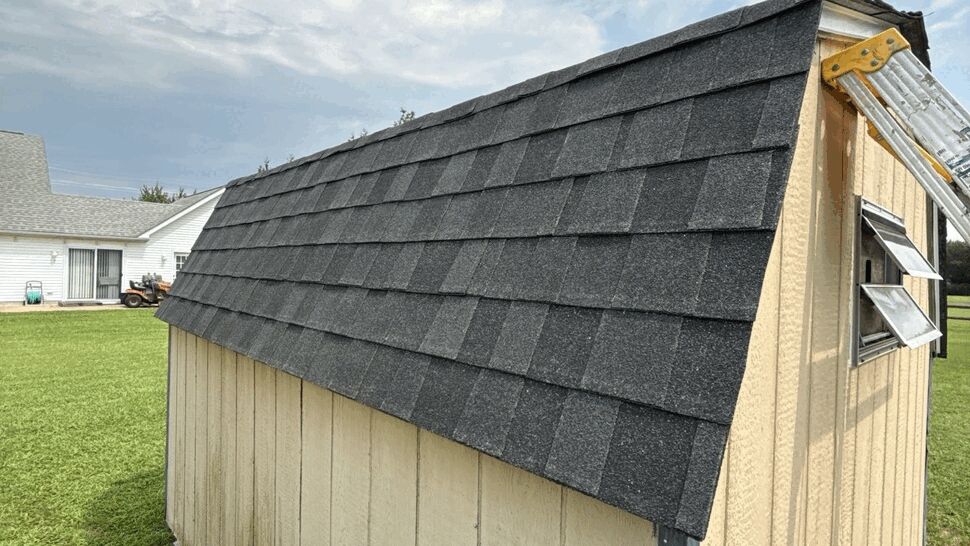 Shed Shingle Roof Installation | Top Roofing & Siding Dark shingle roof installed on a tan outdoor shed beside a home.