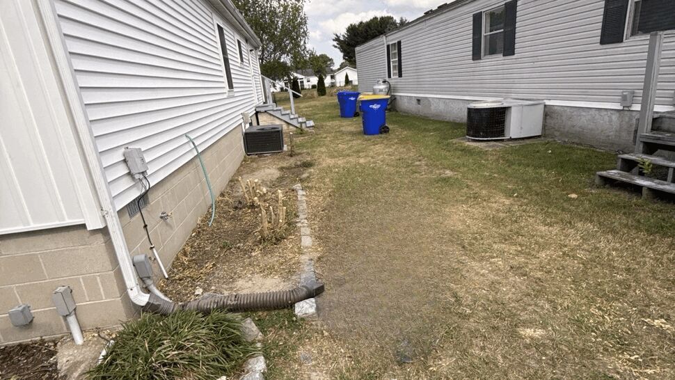 Side yard between homes showing white siding, gutter downspout, and drainage hose