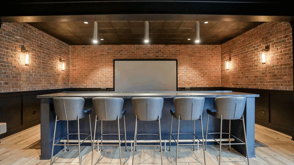 Long bar counter facing a projector screen with high-back stools.