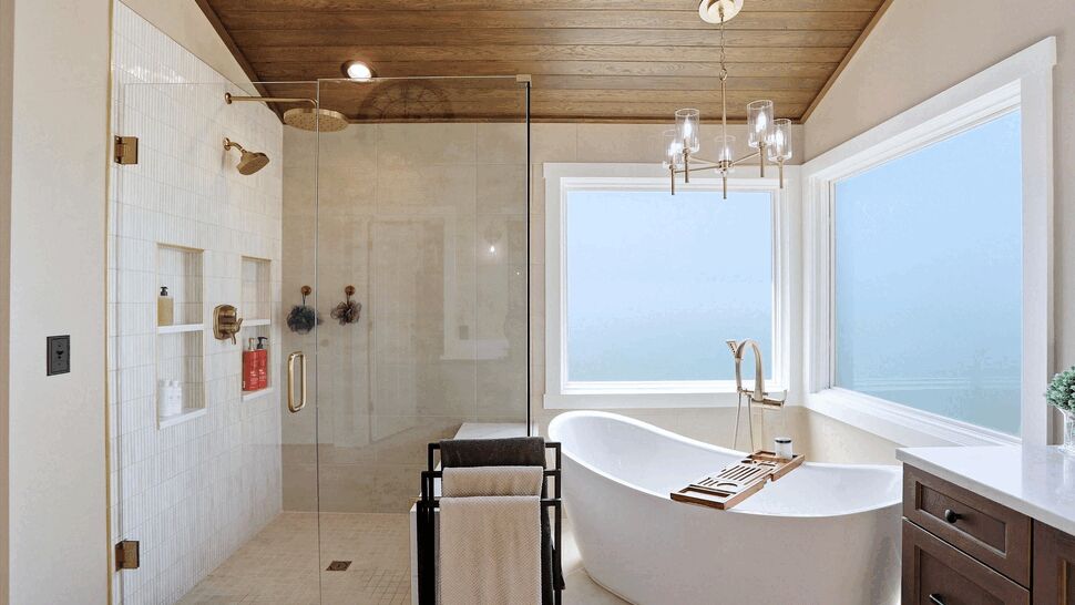 Freestanding tub beside a glass shower with large windows and a chandelier.