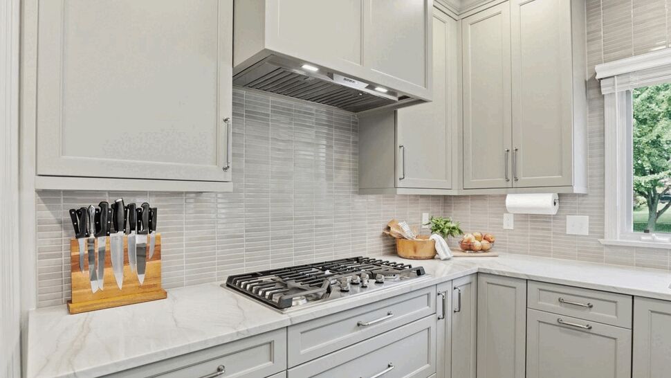 Gas cooktop and hood framed by custom gray cabinets and knife block