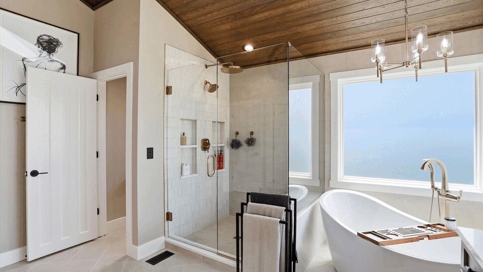 Bright bathroom with glass shower and freestanding tub under a wood-paneled ceiling.