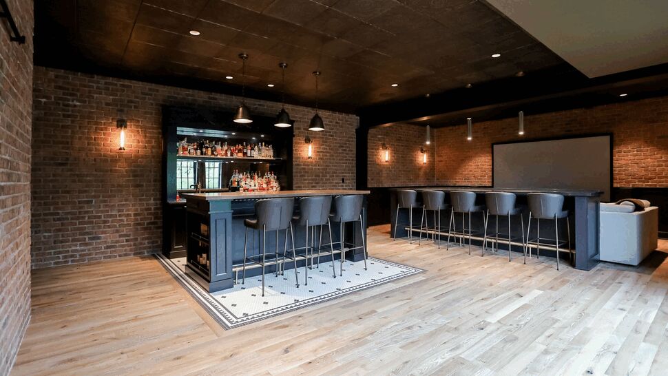 Spacious home bar with light hardwood floors, brick walls, and a central bar island