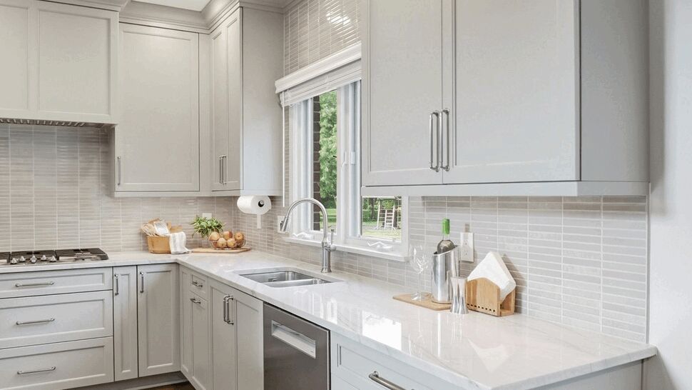 Kitchen sink under window with marble countertop and gray cabinets
