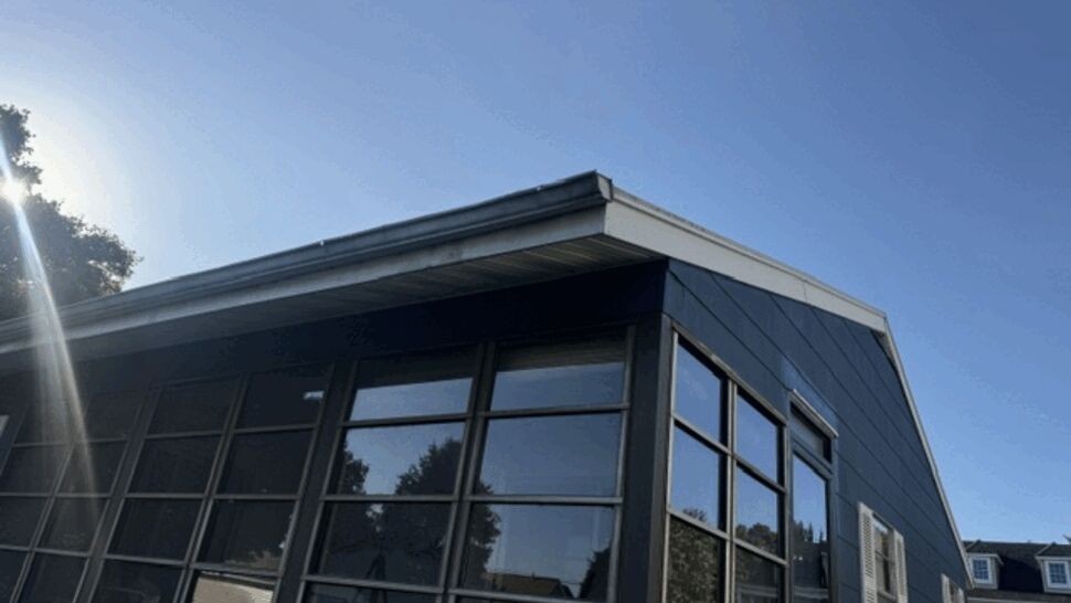 Angled corner of a blue house showing roof edge, soffit and large windows