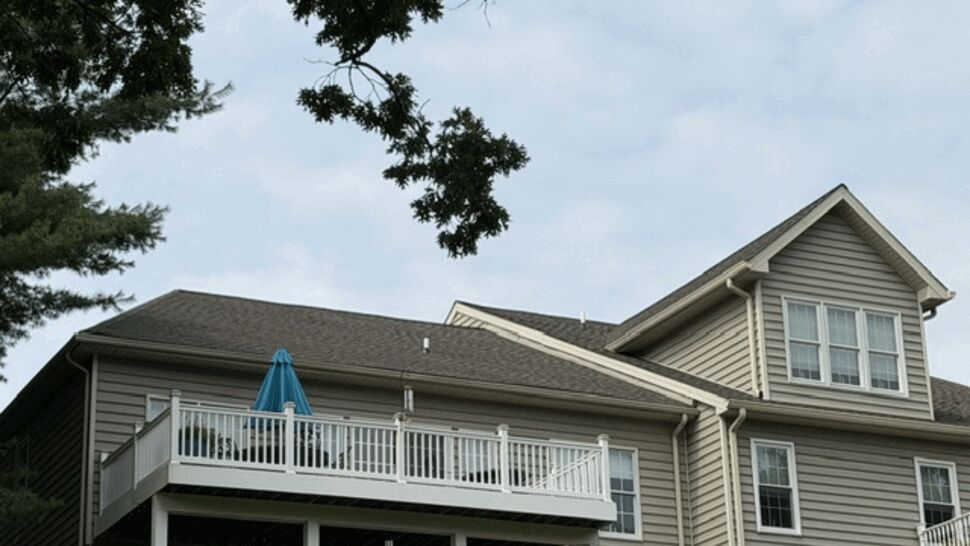 Rear deck and balcony on beige-sided house with visible gutters.