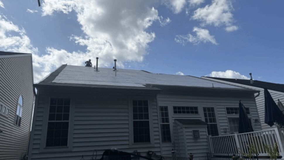 Rear roof stripped to underlayment with workers silhouetted on top.