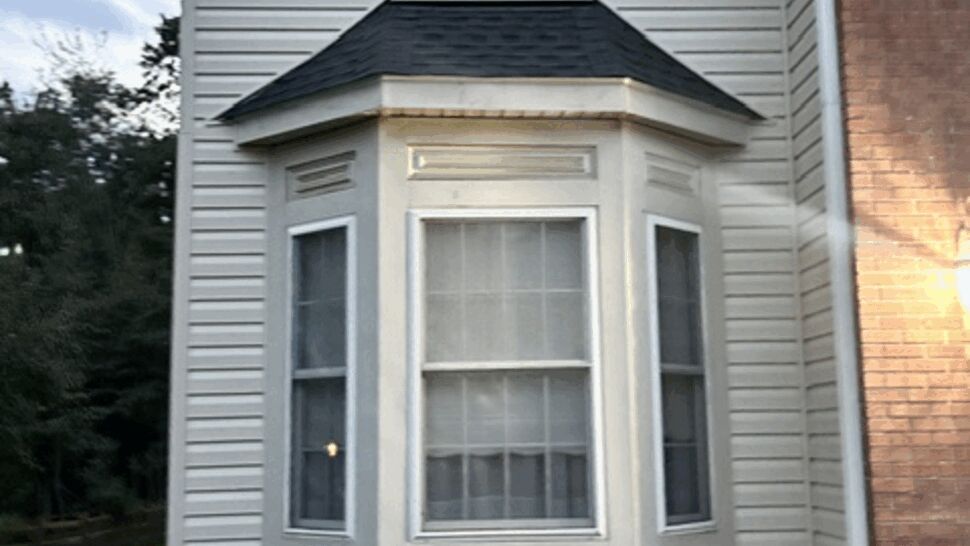 Close-up of bay window with cream siding and small shingled roof
