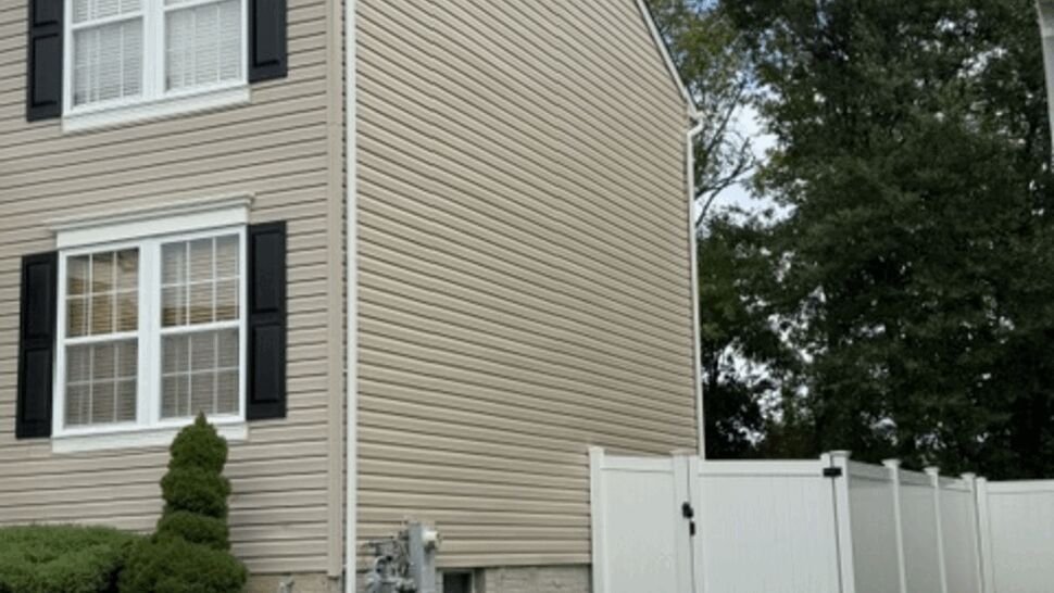 Beige vinyl siding on side of house with white fence and green lawn.