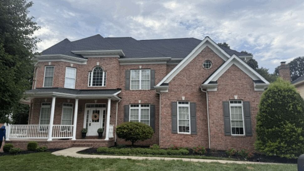 Two-story brick house front with dark shingle roof and white porch.