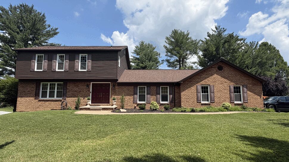 Front view of brick two-story home with brown roof and manicured lawn