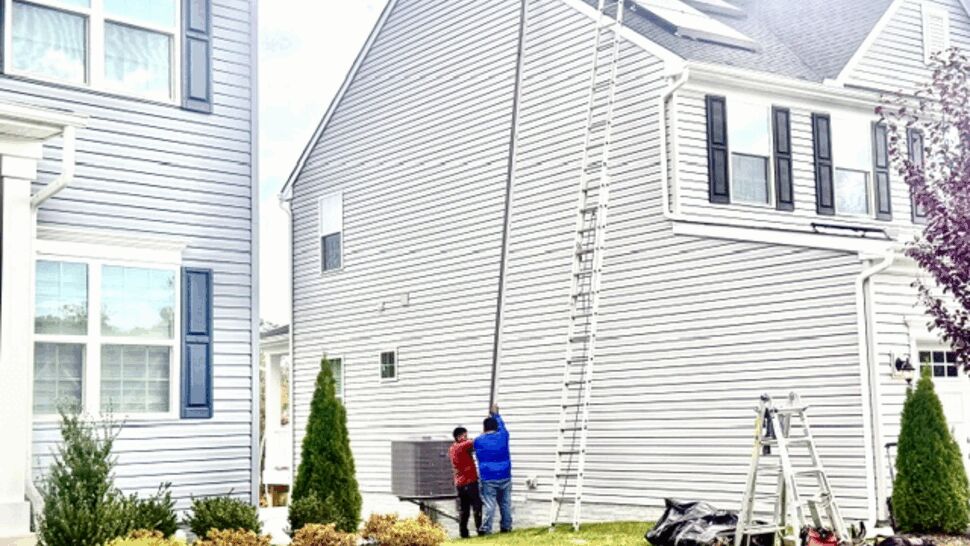 Fresh light gray siding covering a home exterior with workers and equipment nearby