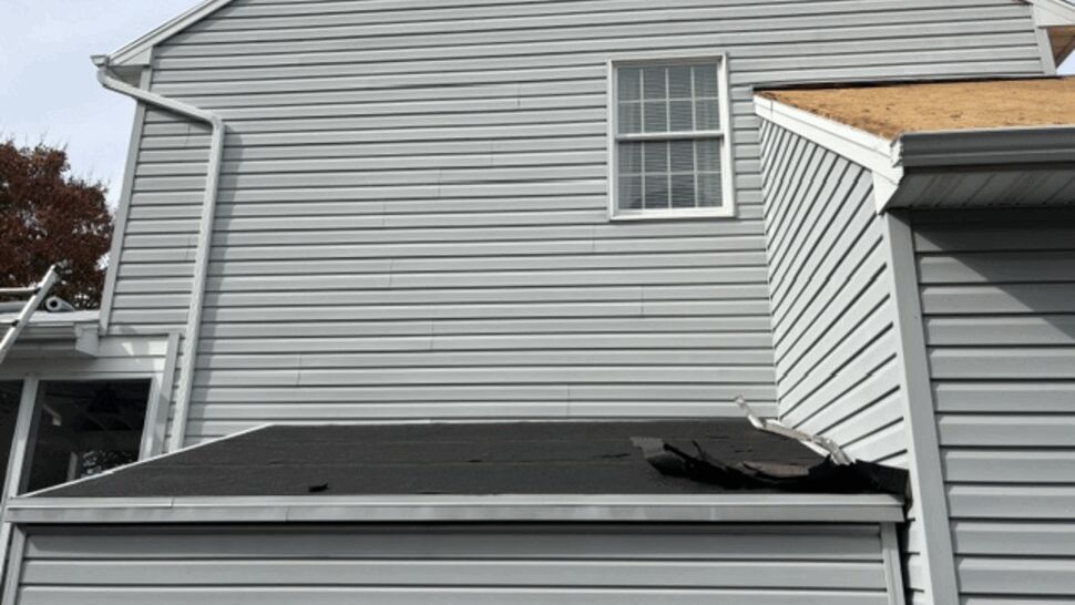Large tear visible in shingles above a garage roof.