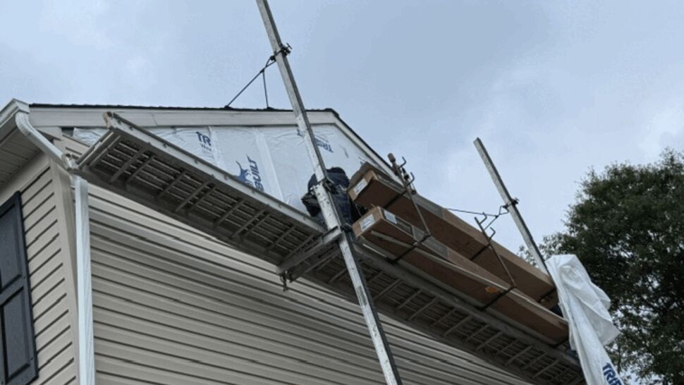Close-up of scaffold at roof eave with workers and roofing materials.