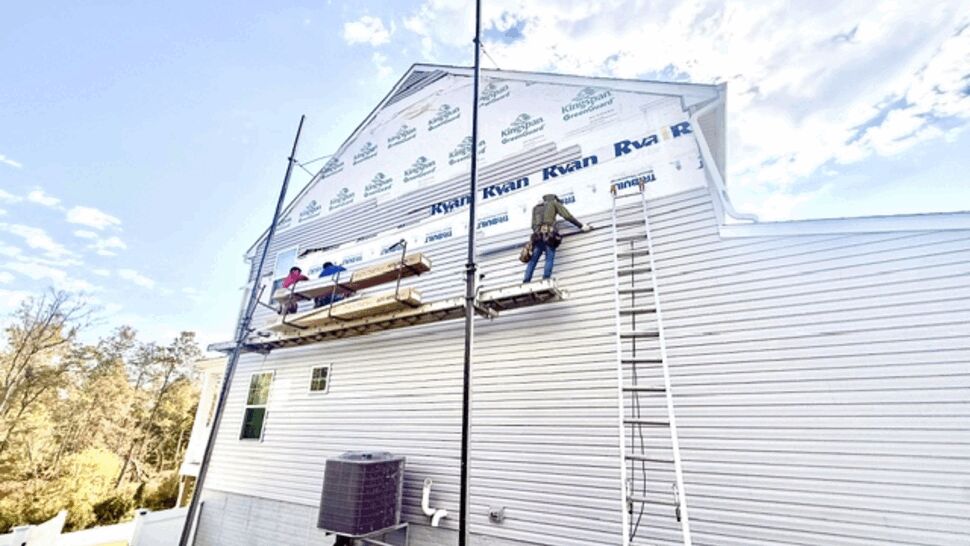 Workers installing siding panels on the rear wall of a two-story home